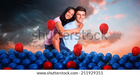 Young man giving girlfriend a piggyback ride against orange and blue sky with clouds