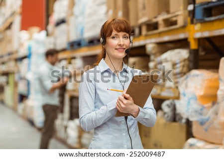 Warehouse manager writing on clipboard in a large warehouse