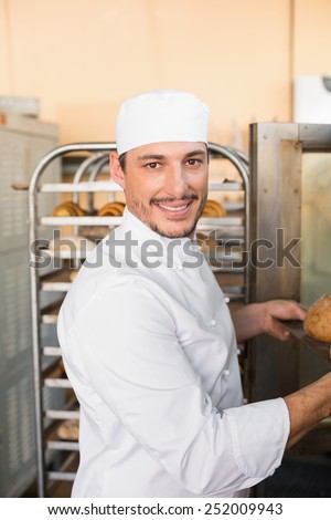 Happy baker taking out fresh loaves in the kitchen of the bakery