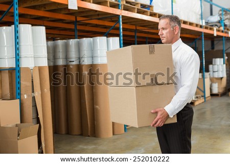 Warehouse manager carrying cardboard boxes in a large warehouse