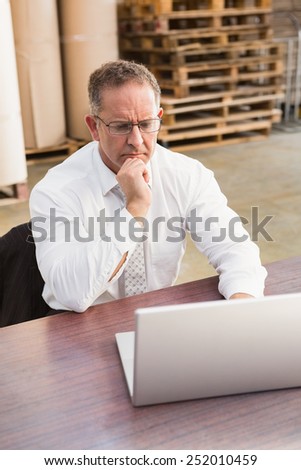 Serious warehouse manager using laptop in a large warehouse