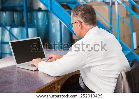 Warehouse manager working on computer in a large warehouse