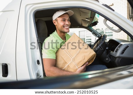 Smiling delivery driver in his van holding parcel outside warehouse