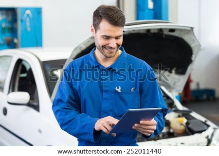 Smiling mechanic using tablet pc at the repair garage