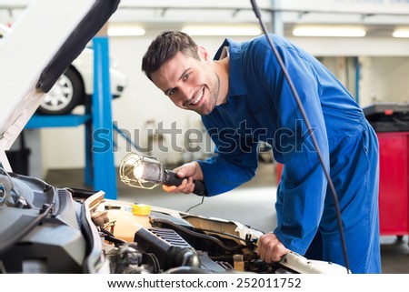 Mechanic examining under hood of car with torch at the repair garage