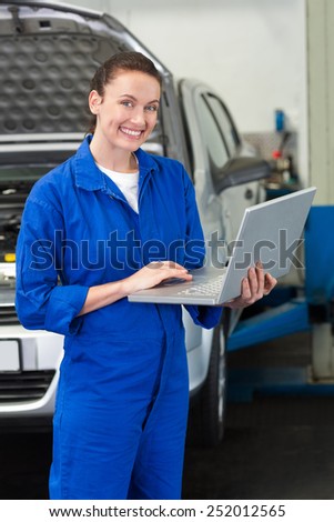 Mechanic smiling at the camera holding laptop at the repair garage