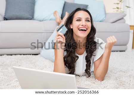 Excited brunette shopping online with laptop at home in the living room