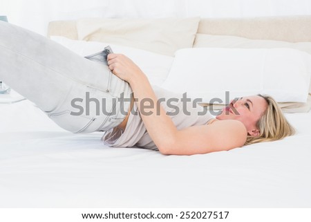 Focused blonde forcing to close her jeans on the bed in hotel room