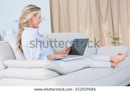 Smiling blonde relaxing on couch with her laptop at home in the living room