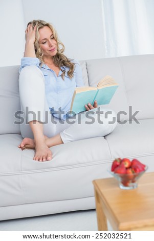 Smiling blonde reading a book on couch at home in the living room