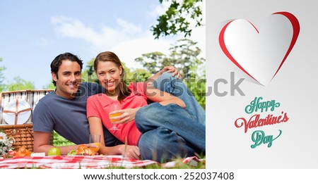 Two friends looking ahead while they hold glasses as they lie on a blanket against cute valentines message