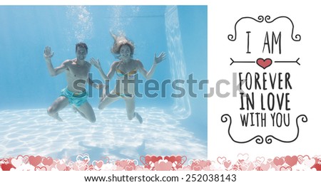 Cute couple smiling at camera underwater in the swimming pool against valentines message