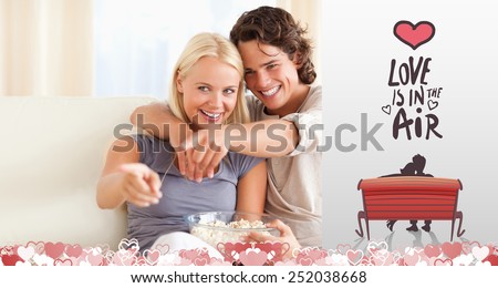 Cute couple watching TV while eating popcorn against love is in the air