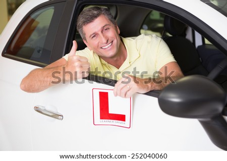 Man gesturing thumbs up holding a learner driver sign at new car showroom