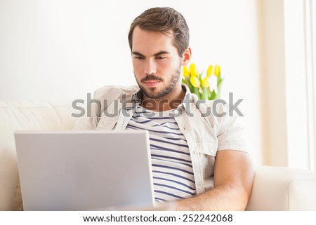 Hipster man using laptop on couch at home in the living room
