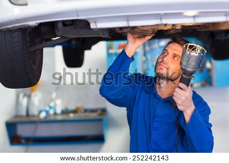 Mechanic examining under the car with torch at the repair garage