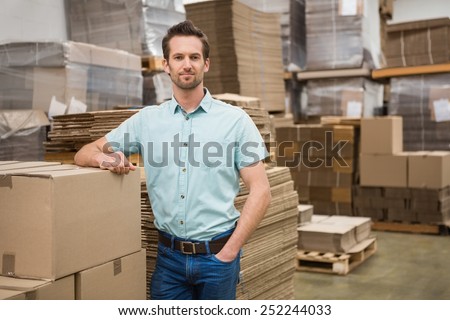 Smiling warehouse worker leaning against boxes in a large warehouse