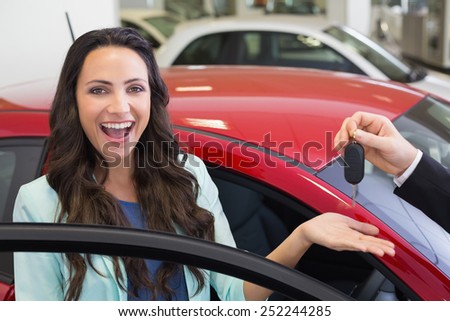 Excited woman receiving car key at new car showroom