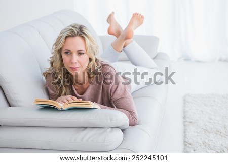Thoughtful lying on couch reading book at home in the living room