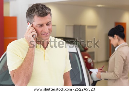 Smiling customer calling with his mobile phone at new car showroom