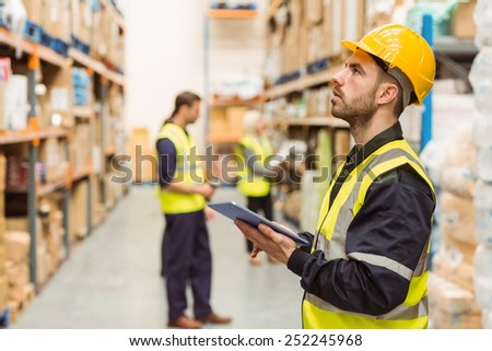 Focused warehouse manager writing on clipboard in a large warehouse