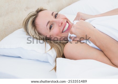 Happy woman lying in bed under duvet at home in the bedroom