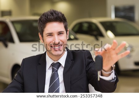 Smiling salesman giving a customer car keys at new car showroom