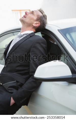 Upset businessman leaning on his car in a car park