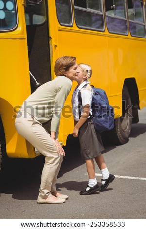 Mother kissing her daughter by school bus outside the elementary school