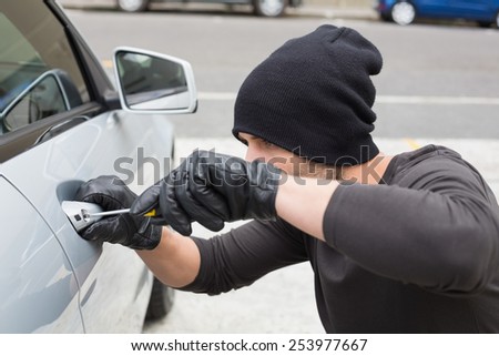 Thief breaking into car with screwdriver in broad daylight