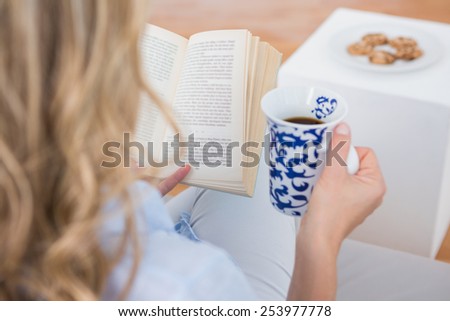 Blonde sitting on couch reading with cup of coffee at home in the living room