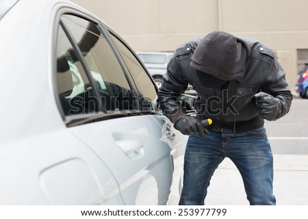 Thief breaking into car with screwdriver in broad daylight