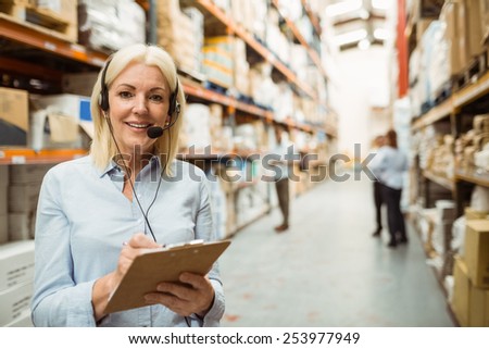 Smiling warehouse manager writing on clipboard in a large warehouse