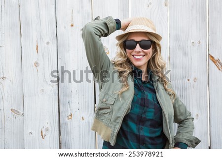 Portrait of blonde in hat posing with sunglasses against bleached wooden planks