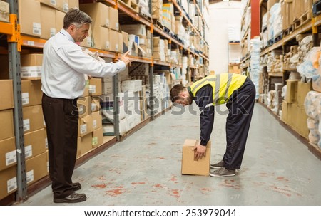 Manager watching worker carrying boxes in a large warehouse