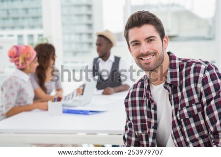 Casual businessman smiling at camera with teamwork behind him