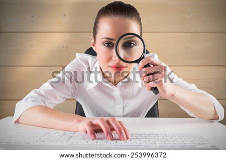 Businesswoman typing and looking through magnifying glass against bleached wooden planks background