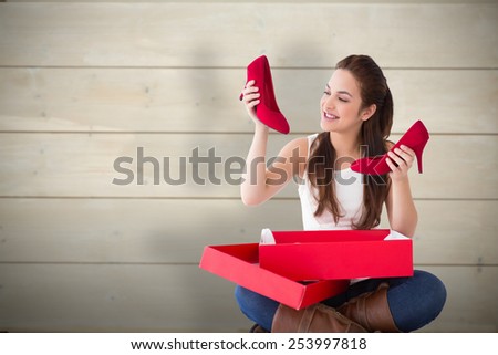 Content brunette holding red shoes against bleached wooden planks background