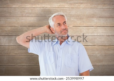 Thinking man posing with hand behind head against wooden surface with planks