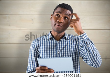 Young businessman thinking and holding tablet against bleached wooden planks background