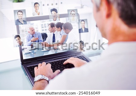 Man with grey hair typing on laptop against group of business people brainstorming together