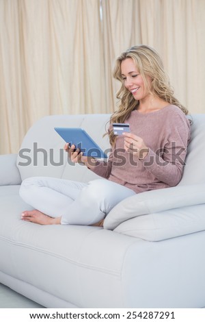 Smiling blonde shopping online with tablet at home in the living room