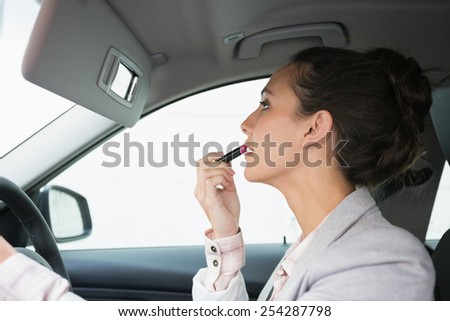 Woman using mirror to put on lipstick while driving in her car