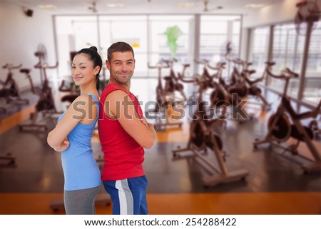 Fit man and woman smiling at camera together against large empty fitness studio with spin bikes