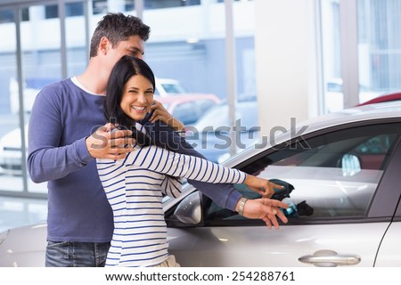 Smiling woman presenting her new car at new car showroom