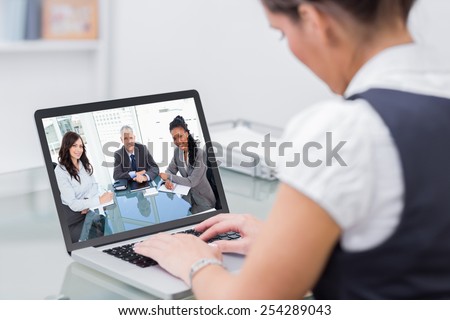 Smiling director sitting at the desk in front of the window between two employees against business worker using laptop at desk