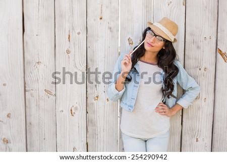 Pretty brunette thinking and smiling against bleached wooden fence