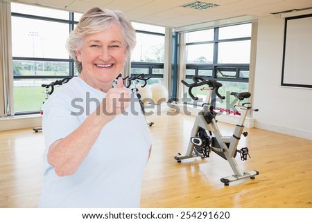 Senior woman showing thumbs up against spinning exercise bikes in gym room