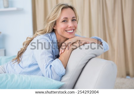 Cheerful pretty blonde sitting on couch at home in the living room