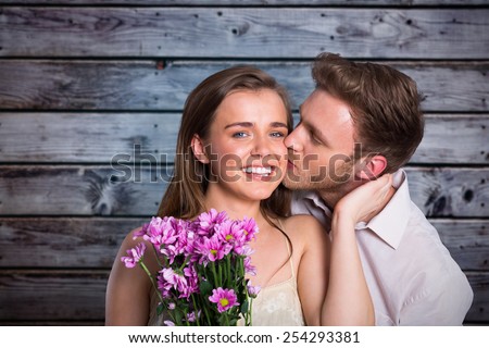 Man kissing woman as she holds flowers against grey wooden planks